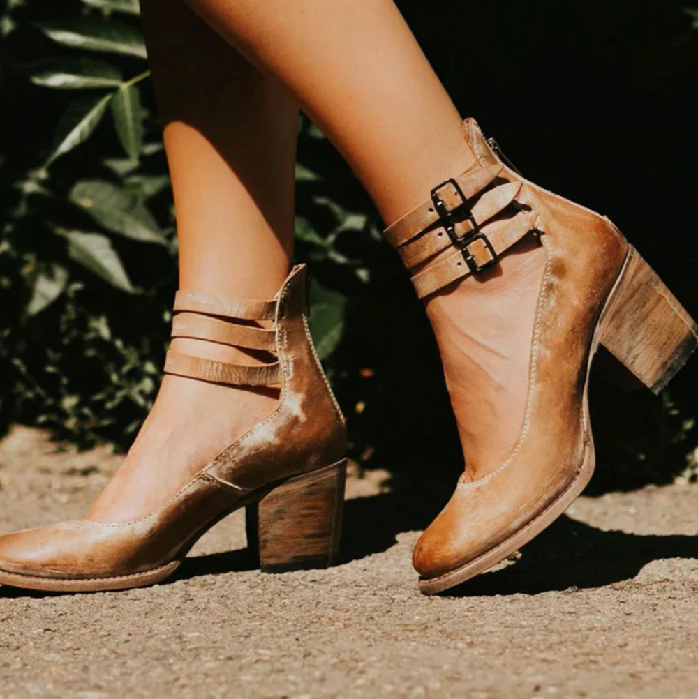 Braune Damenstiefeletten mit Blockabsatz und doppelten Schnallen, stilvoll auf einem sonnigen Gehweg präsentiert. Perfekt für Herbstmode.