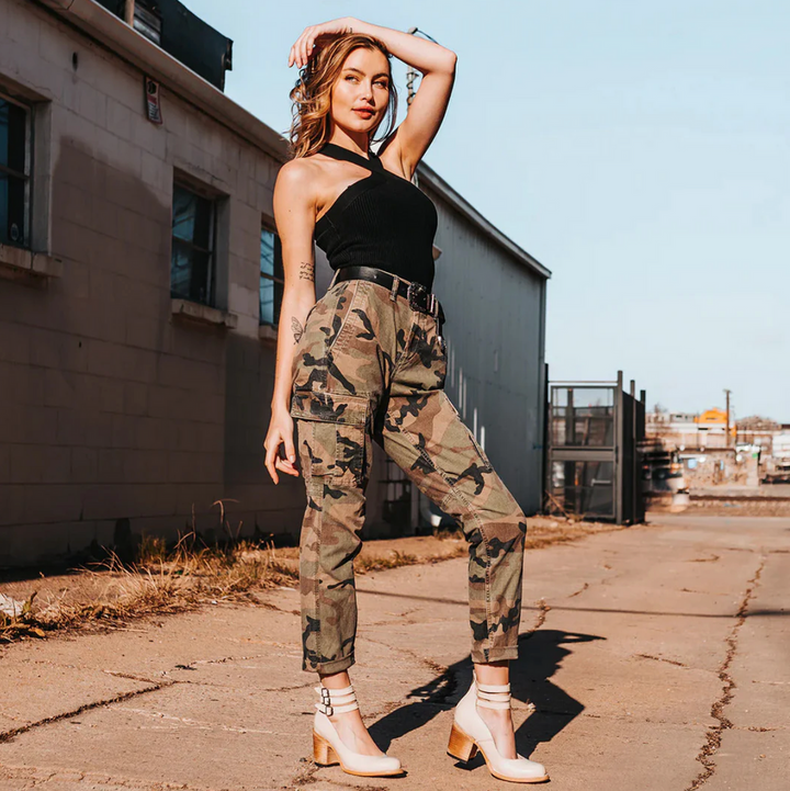Frau in Camouflage-Hose und schwarzem Top posiert auf urbaner Straße. Modetrend, Streetstyle, lässiger Look, Outdoor-Fotografie.