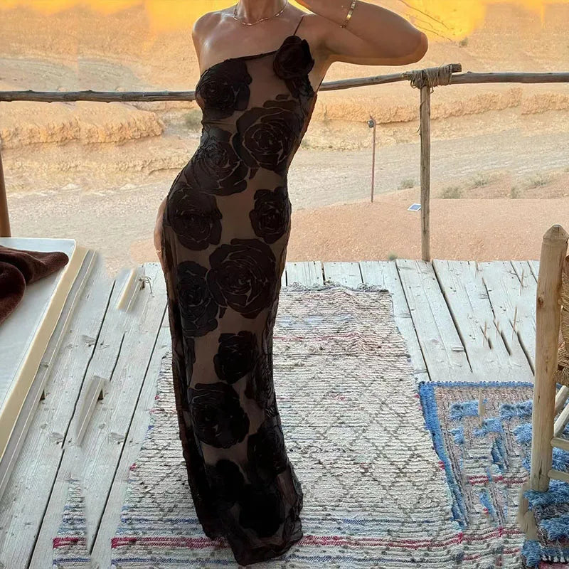 Eine Person trägt ein elegantes, schwarzes, schulterfreies Kleid mit Rosenmuster auf einer Holzterrasse in einer Wüstenlandschaft.