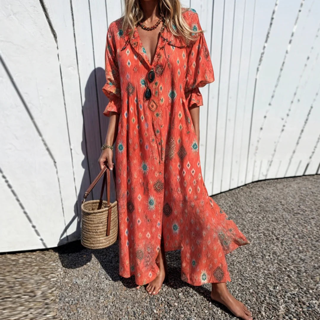 Frau in rotem Boho-Kleid mit Ethno-Muster, trägt Strohtasche, steht vor weißer Holzwand. Sommermode, lässiger Stil, Strandkleid.