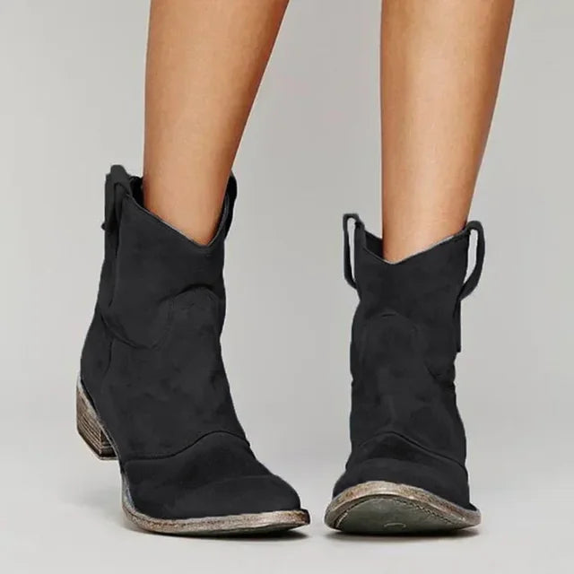 Schwarze Cowboystiefel aus Wildleder mit abgenutzter Sohle, getragen von einer Person. Modische Damenstiefel, ideal für Herbst-Outfits.