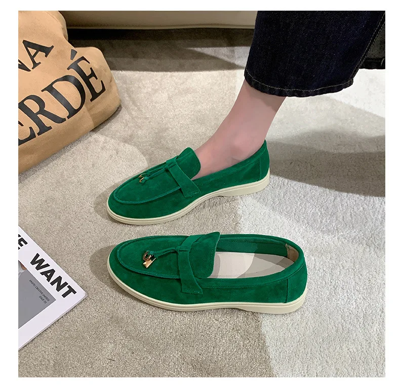 Grüne Wildleder-Loafer mit goldener Schnalle auf beigem Teppich, getragen von Person in dunkler Jeans. Elegante Schuhe, modisches Design.