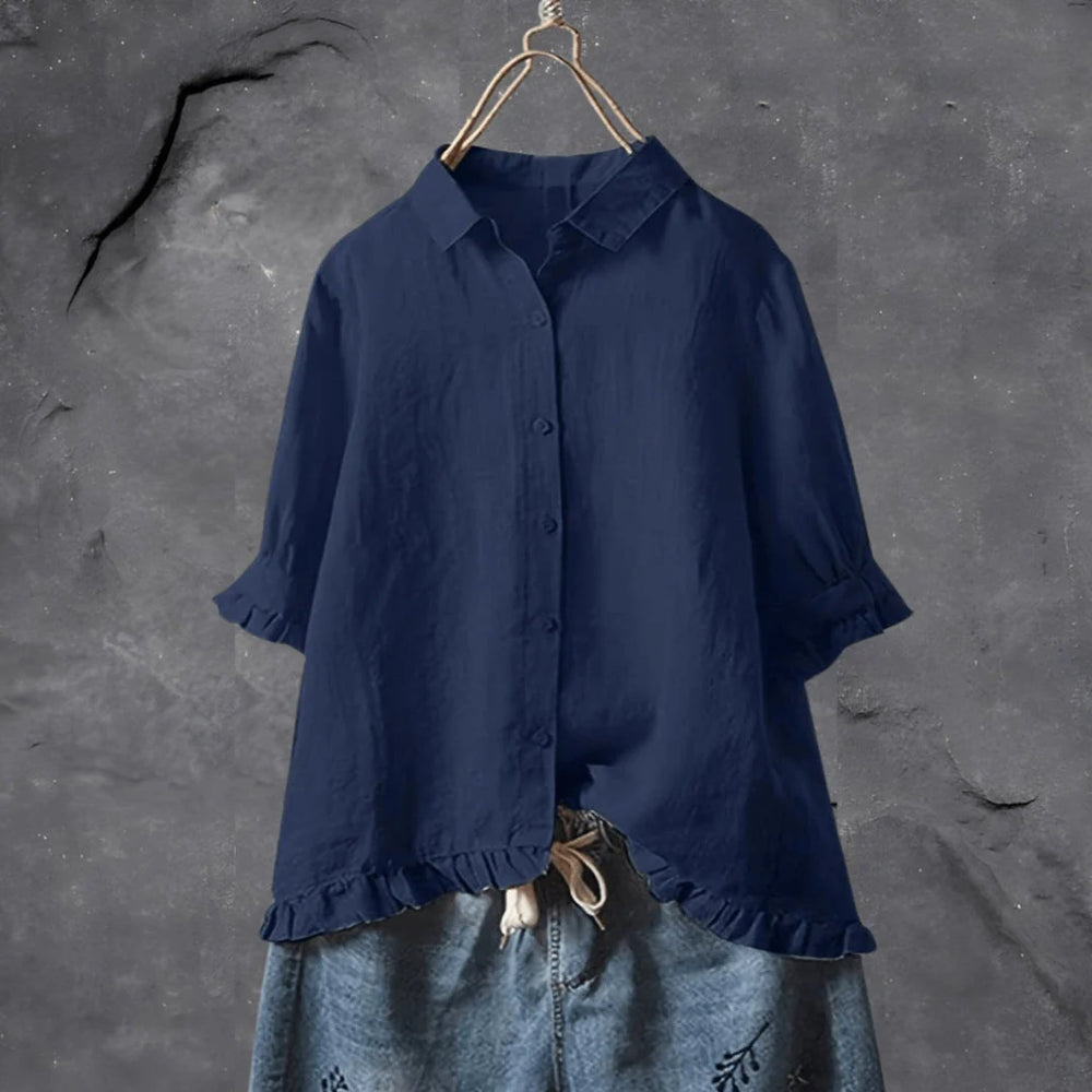 Dunkelblaues Leinenhemd mit Knopfleiste und Rüschen, hängend vor grauem Hintergrund. Modetrend, Damenbekleidung, lässiger Stil.