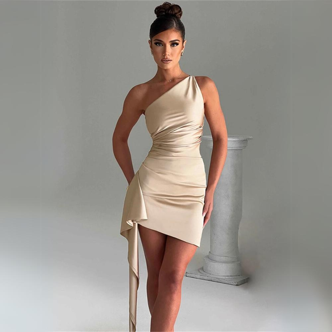 Eine Frau in einem eleganten, einseitigen, beigen Kleid posiert vor einer grauen Kulisse mit einer Säule. Abendmode, Damenkleid, schulterfrei.