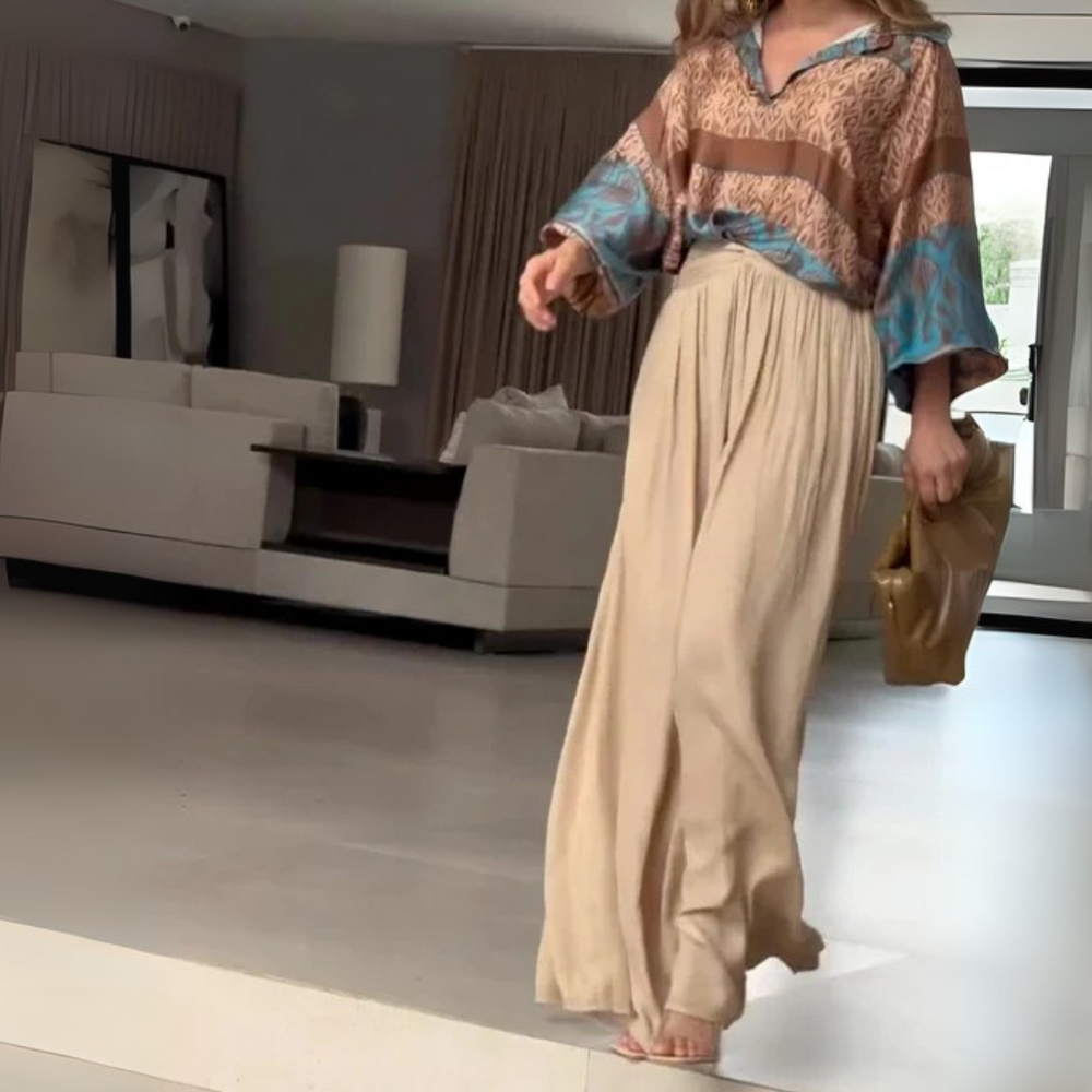 Frau in eleganter, gemusterter Bluse und beiger Hose in modernem Wohnzimmer. Stilvolle Mode, Inneneinrichtung, zeitgenössisches Design.