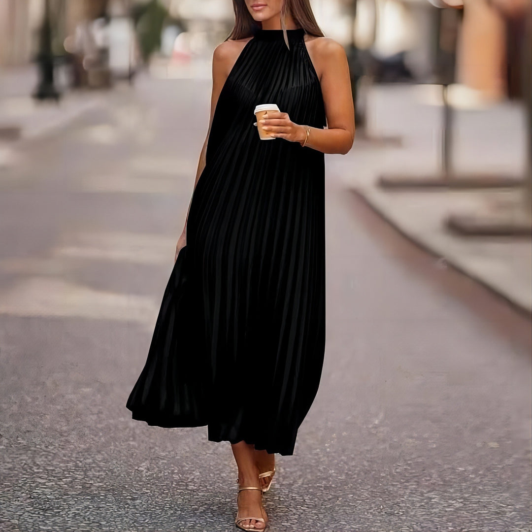 Frau in elegantem, schwarzem, plissiertem Kleid mit Kaffeebecher, spaziert auf städtischer Straße. Mode, Streetstyle, Sommerkleid, urbane Eleganz.
