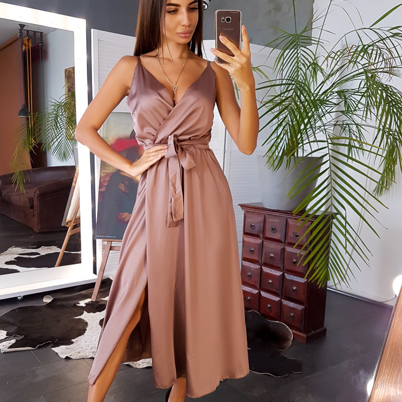 Frau in elegantem, ärmellosem, braunem Kleid posiert vor Spiegel, hält Smartphone. Modernes Schlafzimmer, Pflanzen, Holzmöbel im Hintergrund.