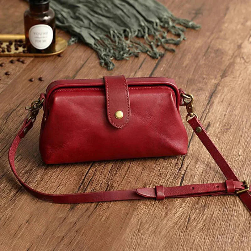 Rote Ledertasche mit verstellbarem Schulterriemen auf Holztisch, umgeben von Kaffeebohnen und grünem Schal. Elegante Damenhandtasche Accessoire.