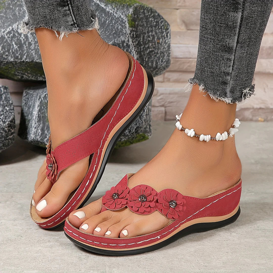 Rote Damen-Sandalen mit Blumenverzierung, getragen mit Jeans und Fußkettchen. Bequeme Sommerschuhe, modisch und stilvoll.