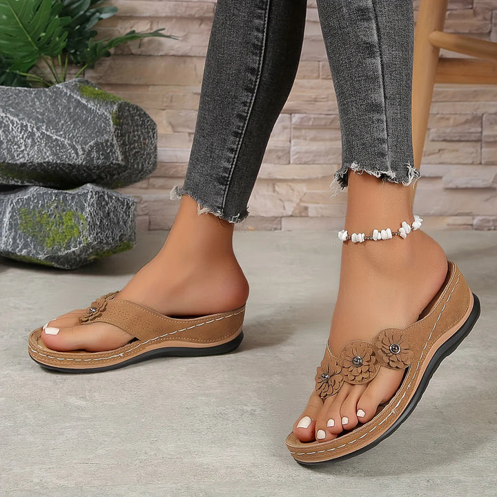 Damenfüße in modischen, braunen Keilsandalen mit Blumenmuster, getragen mit grauen Jeans. Perfekte Sommermode für stilvolle Freizeitoutfits.