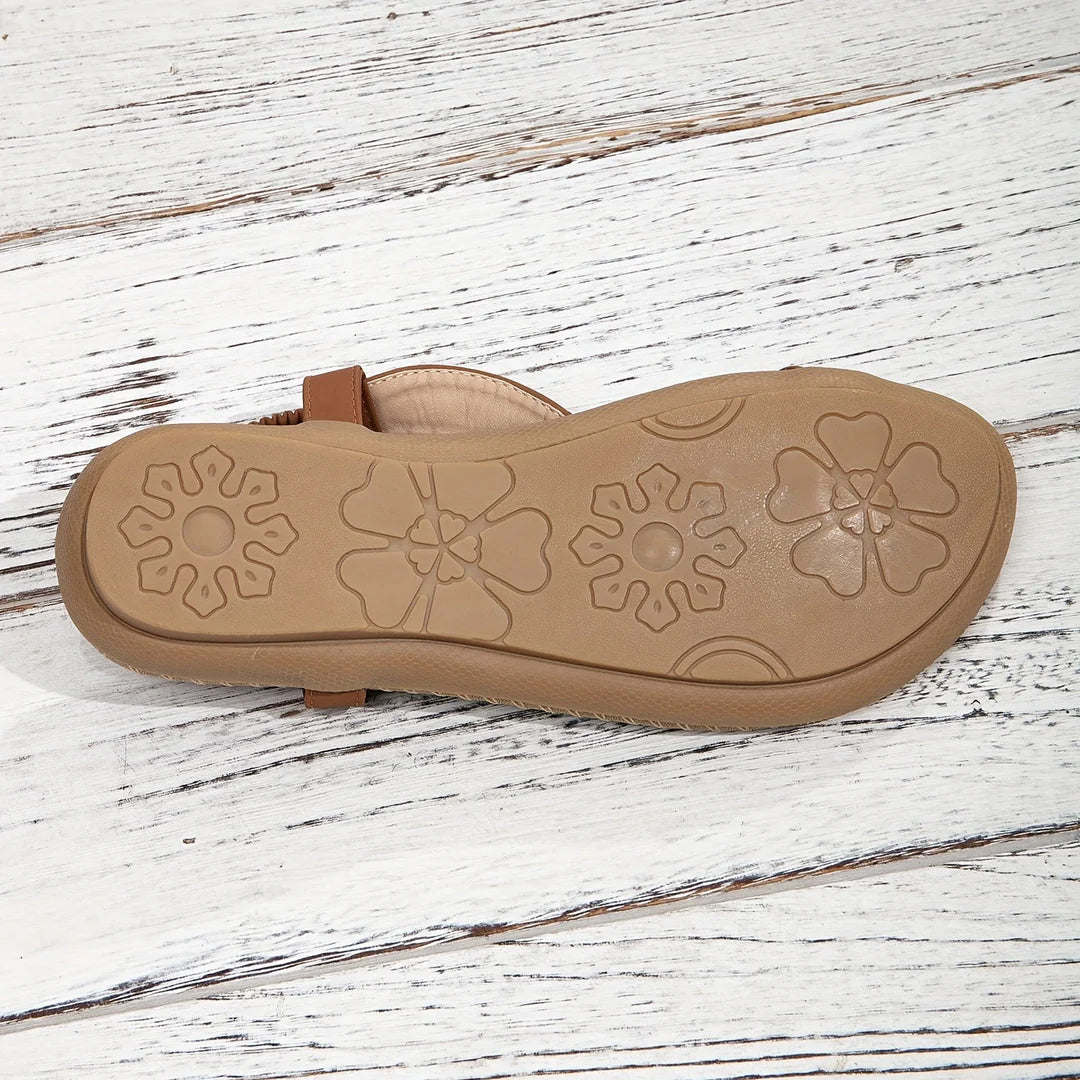 Braune Sandale mit floralem Muster auf der Sohle, auf weißem Holzuntergrund. Bequeme Sommerschuhe, rutschfeste Sohle, modisches Design.