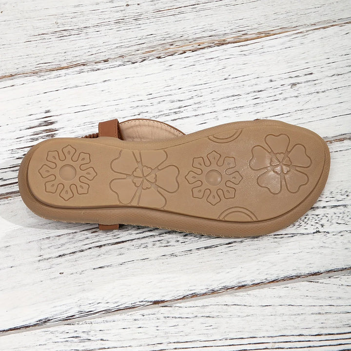 Braune Sandale mit floralem Muster auf der Sohle, auf weißem Holzuntergrund. Bequeme Sommerschuhe, rutschfeste Sohle, modisches Design.