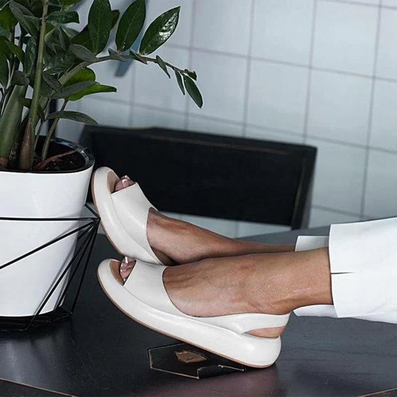 Weiße Sandalen mit offener Spitze auf einem Tisch neben einem Blumentopf. Bequeme Sommerschuhe, modernes Design, ideal für Freizeit und Büro.