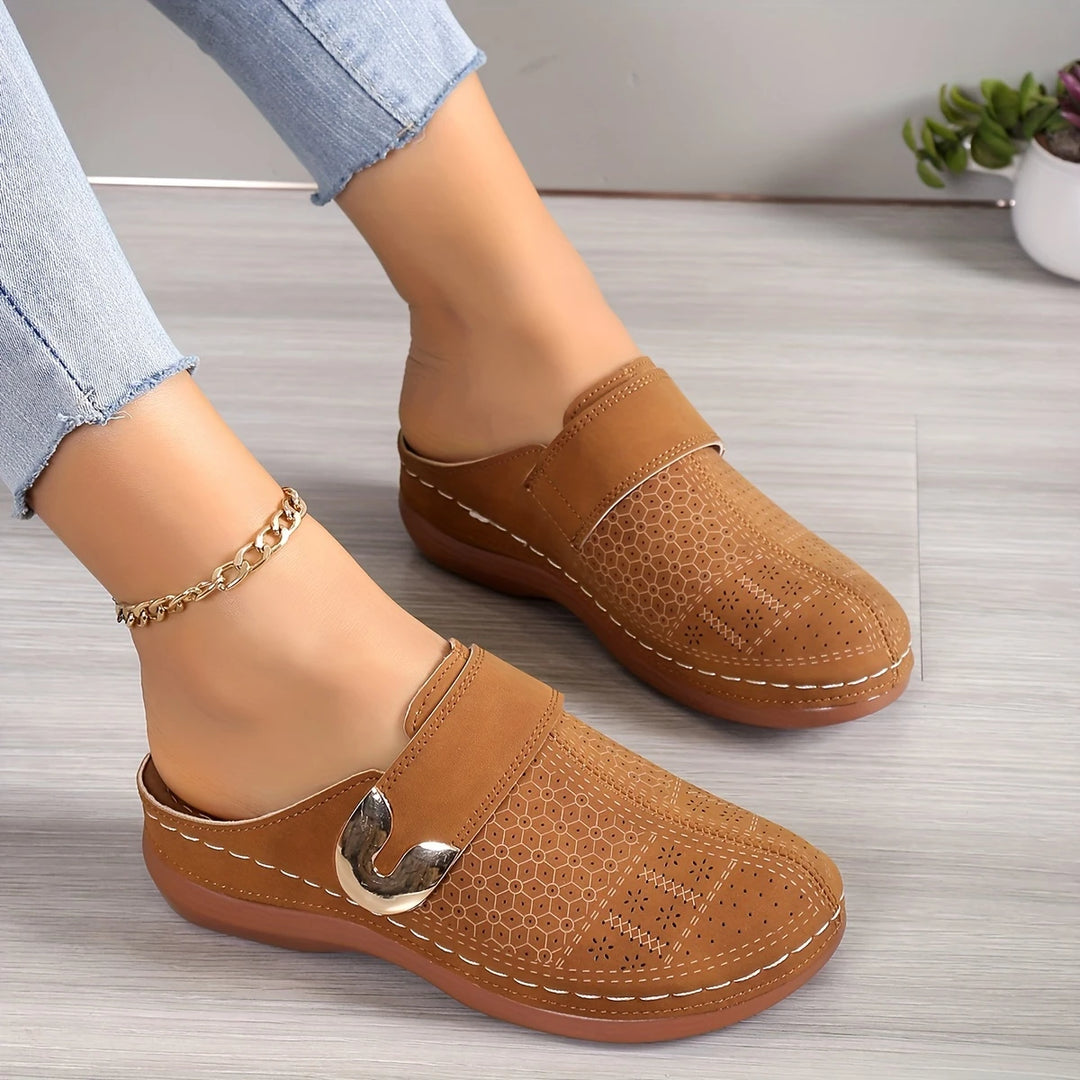 Damen Clogs in Braun mit perforiertem Muster und goldener Schnalle, kombiniert mit blauer Jeans. Bequeme Schuhe für Alltag und Freizeit.