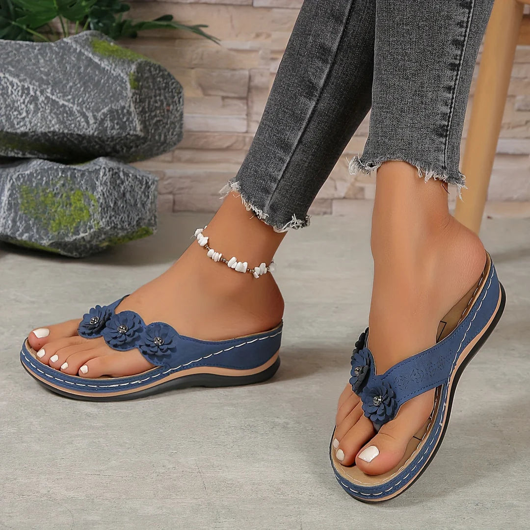 Frau trägt blaue Sandalen mit Blumenmuster, Jeans mit Fransen. Modische Sommerschuhe, bequeme Flip-Flops, Damenmode, Freizeitlook.