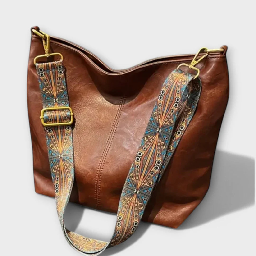 Braune Ledertasche mit verziertem, buntem Schultergurt auf grauem Hintergrund. Modische Damenhandtasche, ideal für Alltag und Freizeit.