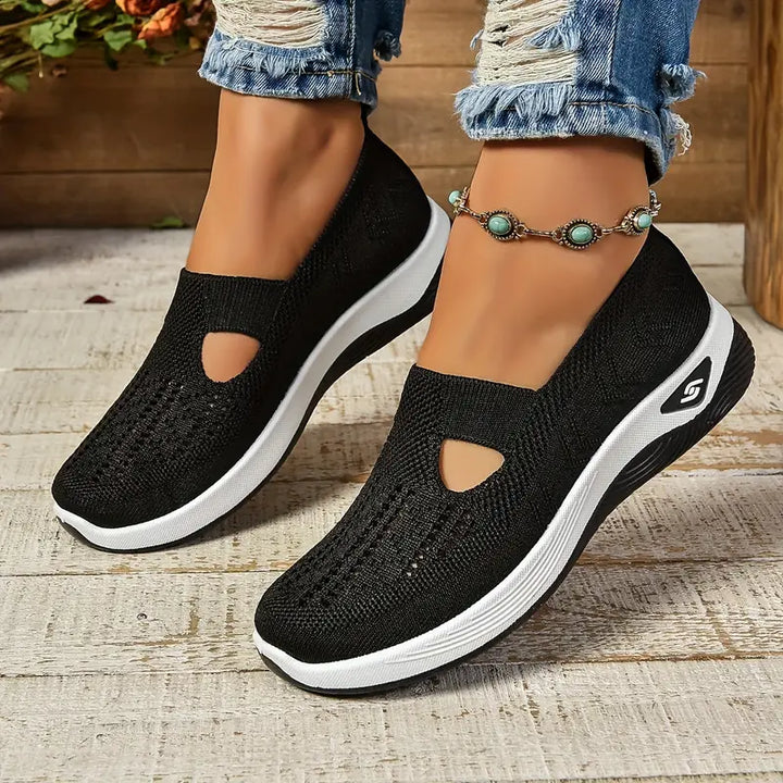 Schwarze Damen-Sneaker mit weißer Sohle, atmungsaktivem Strickmaterial und Cut-Out-Design, getragen mit zerrissenen Jeans und türkisfarbenem Fußkettchen.