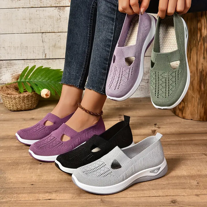 Frau probiert bequeme, atmungsaktive Slip-On-Sneaker in Lila, Schwarz, Grau und Grün an. Modische Damen-Schuhe auf Holzboden.