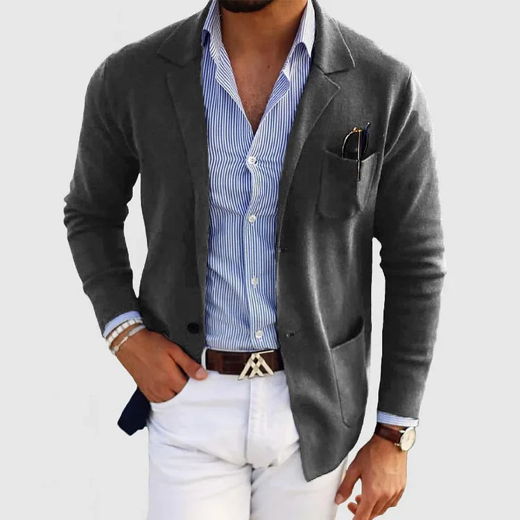 Mann in grauem Blazer, blau-weiß gestreiftem Hemd und weißer Hose, modisch elegant gekleidet, mit Armbanduhr und Einstecktuch.