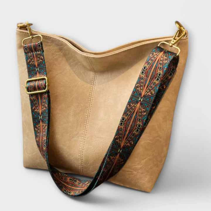 Beige Handtasche mit verstellbarem, gemustertem Schultergurt auf weißem Hintergrund. Modische Damenaccessoire, ideal für Alltag und Freizeit.