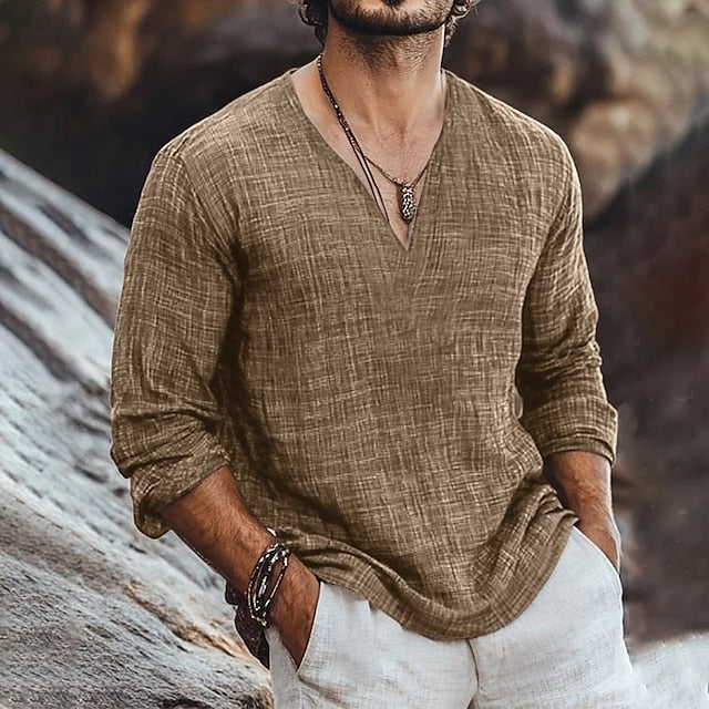 Mann in braunem Leinenhemd und weißer Hose, lässig an Felsen gelehnt. Modetrend, Herrenbekleidung, Freizeitlook, Naturkulisse.