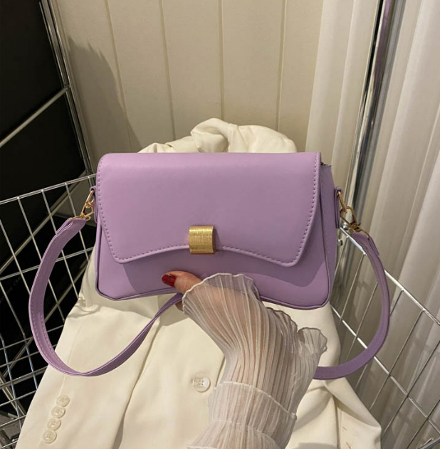 Lila Handtasche mit goldener Schnalle, gehalten von Hand in weißem Rüschenärmel, auf weißem Stoffhintergrund. Elegante Damenmode Accessoire.