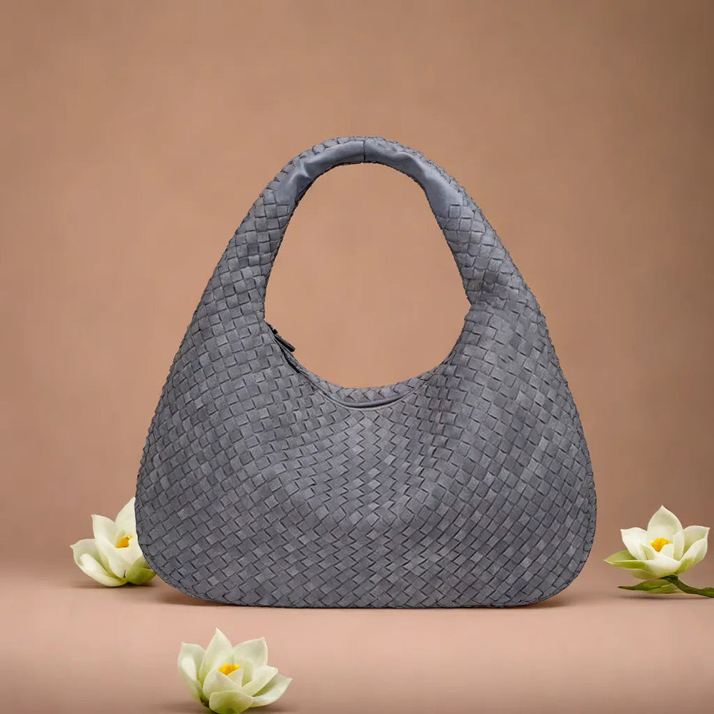 Graue geflochtene Handtasche auf beigem Hintergrund mit weißen Blumen. Modische Damenaccessoire, elegantes Design, ideal für stilvolle Outfits.