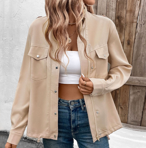 Frau trägt beige Hemdjacke, weißes Crop-Top und blaue Jeans. Modetrend, lässiger Stil, Damenmode, Herbstoutfit, Streetwear-Look.