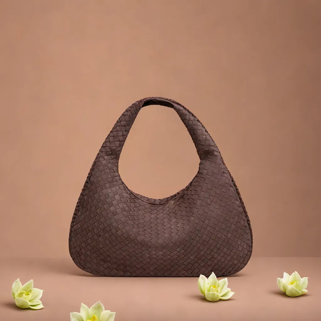 Braune geflochtene Handtasche vor beigem Hintergrund, umgeben von weißen Lotusblüten. Elegante Damenmode, stilvolles Accessoire, modische Tasche.