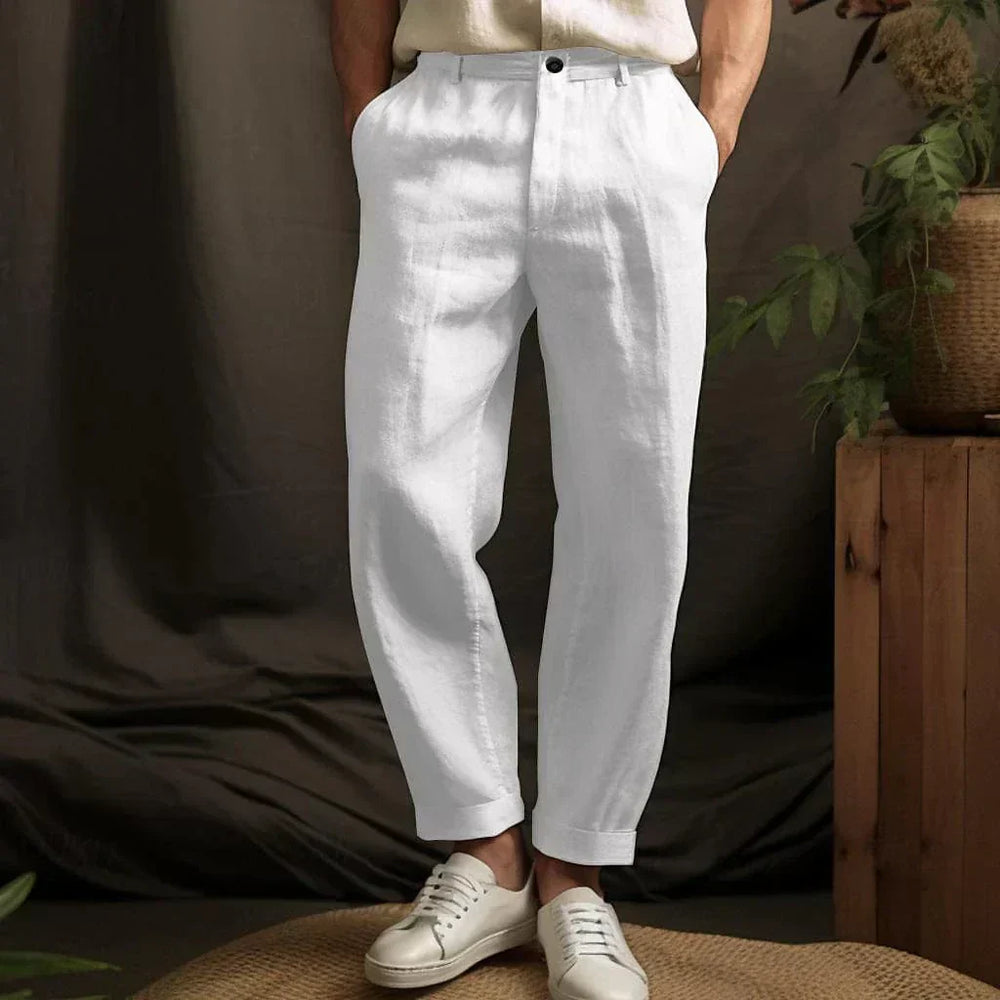 Weiße Leinenhose für Herren, kombiniert mit weißen Sneakers, vor einem Hintergrund mit Pflanzen. Ideal für Sommermode und lässigen Stil.