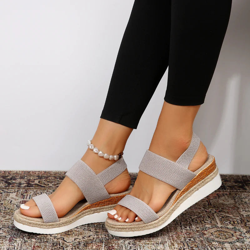 Damen Sandalen mit Keilabsatz, beige, elastische Riemen, bequem, modisch, ideal für Sommer, kombiniert mit schwarzer Leggings und Perlenfußkettchen.
