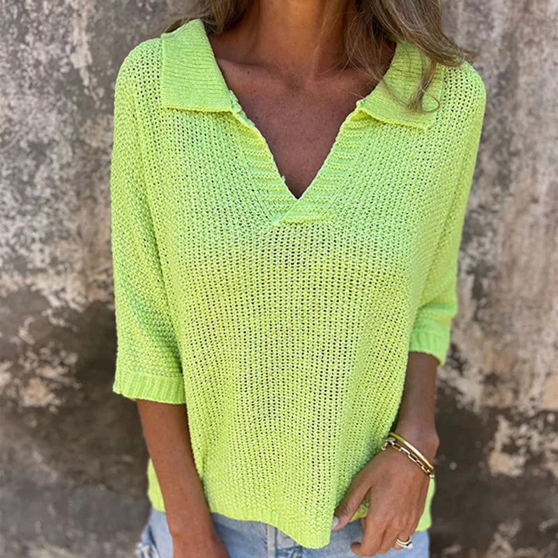 Frau trägt leuchtend gelben Strickpullover mit V-Ausschnitt und Dreiviertelärmeln vor rustikalem Hintergrund. Modetrend, Damenmode, Strickmode.