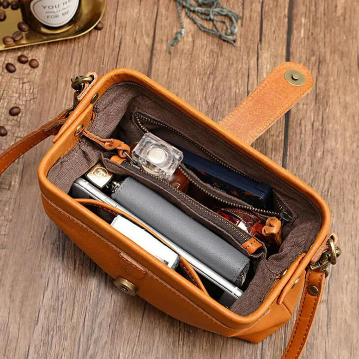 Kleine braune Ledertasche auf Holztisch, geöffnet mit Smartphone, Notizbuch, Lippenstift und Schlüssel. Stilvolle Damenhandtasche, Alltagsgegenstände.