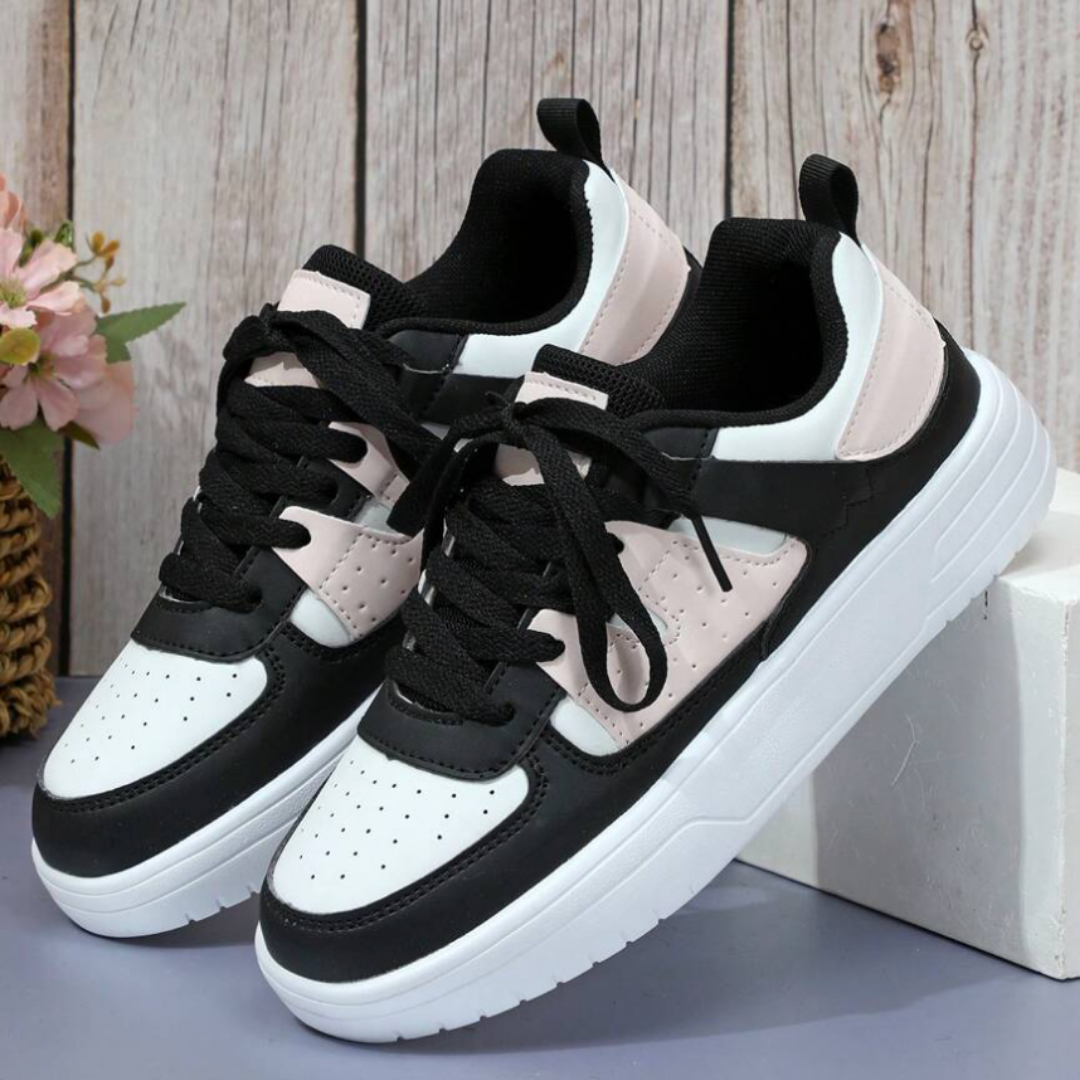 Schwarz-weiße Sneaker mit rosa Akzenten auf weißem Podest vor Holzwand. Modische Turnschuhe, ideal für Freizeit und Sport.