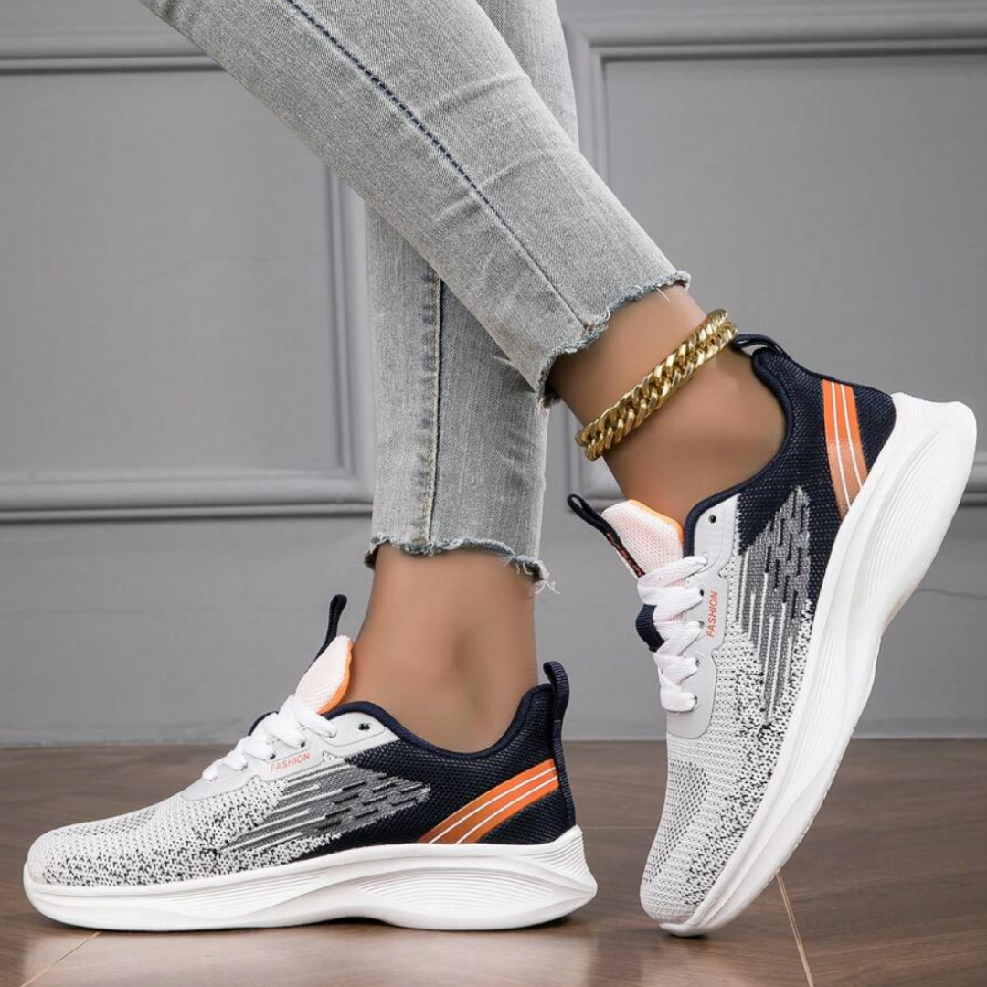 Damen Sneaker in Weiß und Schwarz mit orangefarbenen Akzenten, getragen mit hellblauen Jeans. Modische Sportschuhe, ideal für Freizeit und Sport.