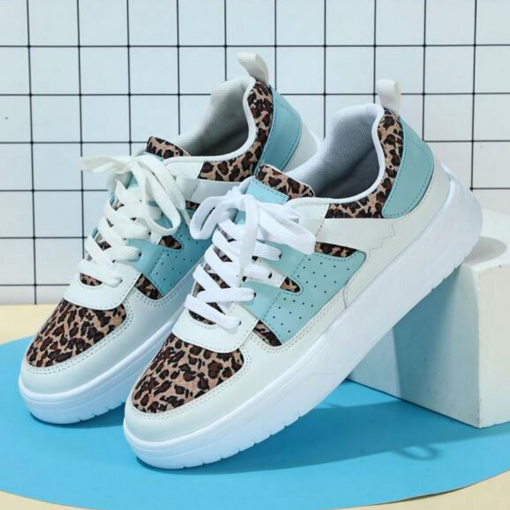 Leopard-Sneaker mit weißer Sohle und türkisfarbenen Akzenten vor kariertem Hintergrund. Modische Turnschuhe, trendiges Design, Damenmode.