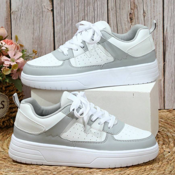 Weiße und graue Sneaker auf Holzhintergrund, modisch und sportlich, mit Blumenarrangement. Ideal für Freizeit und Streetwear.