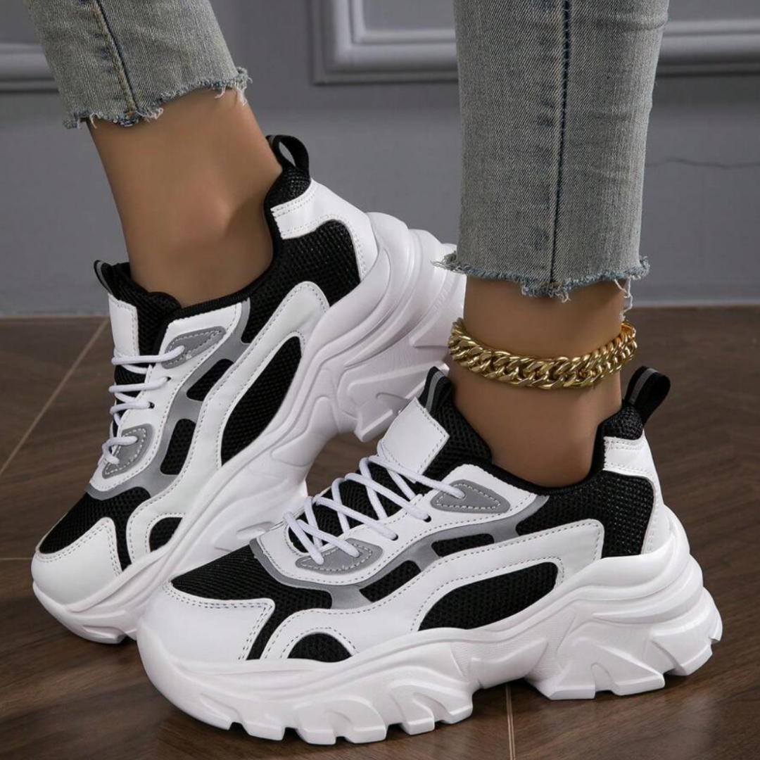 Damen Sneaker in Schwarz-Weiß, klobiges Design, kombiniert mit hellblauen Jeans und goldener Fußkette, modischer Streetwear-Look.